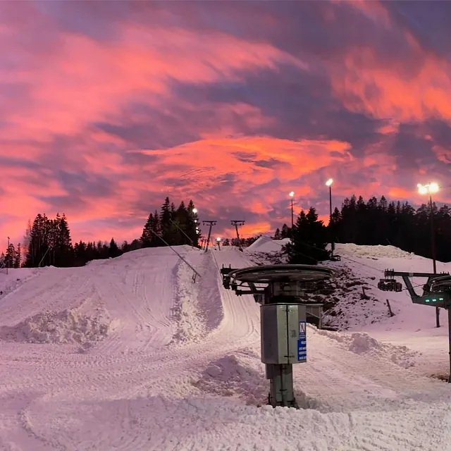 Skitrekk og snødekte bakker i dramatisk solnedgang med rødfarget himmel.