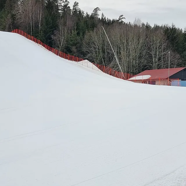 Bred og nypreparert alpinbakke med sikkerhetsnett og tråkkemaskin i bakgrunnen.