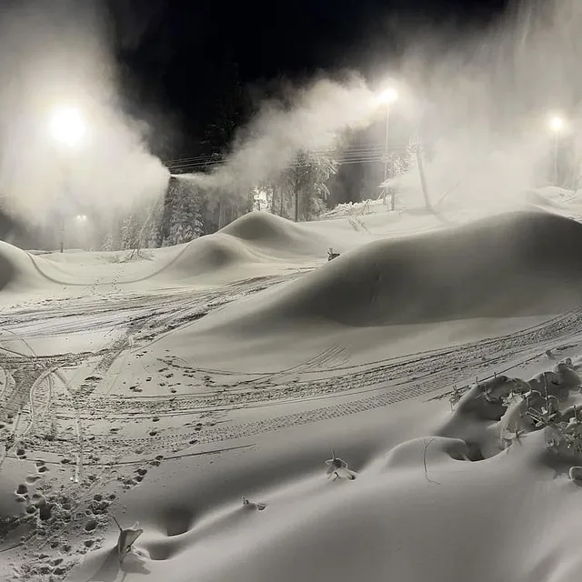 Snøkanoner i drift om natten med store snøhauger i bakken.