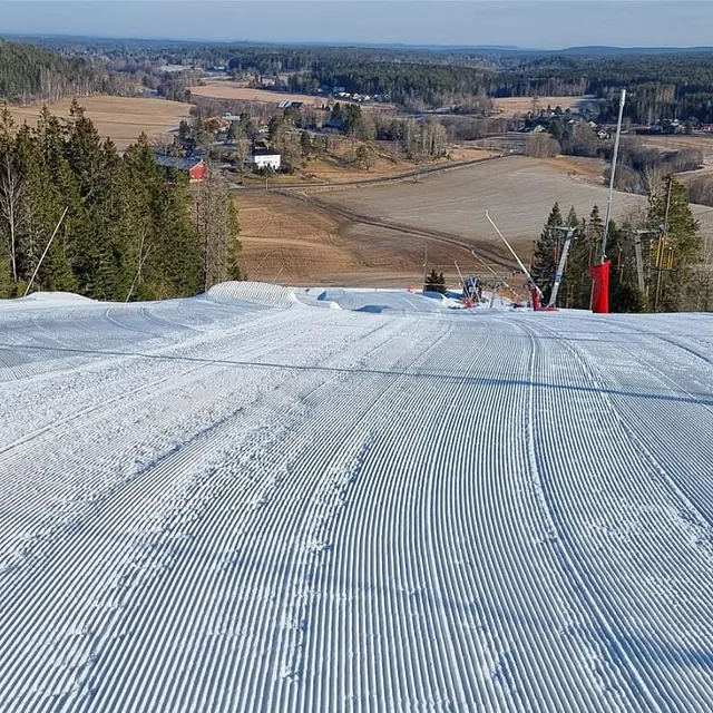 Nypreparert alpinbakke med utsikt over jordbrukslandskap og skog i bakgrunnen.