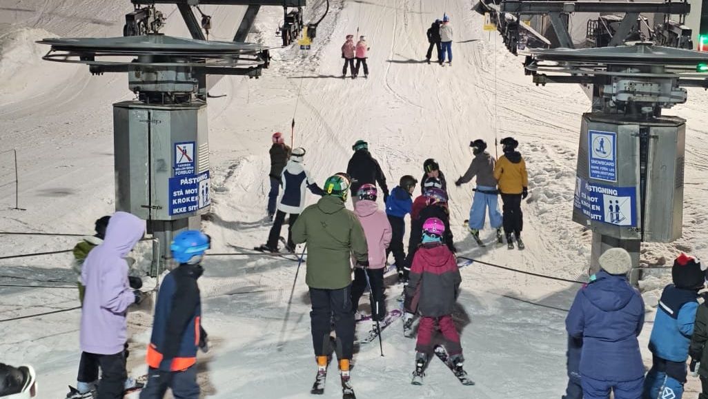 Skikø ved heisanlegg om kvelden med barn og voksne klare for bakken.